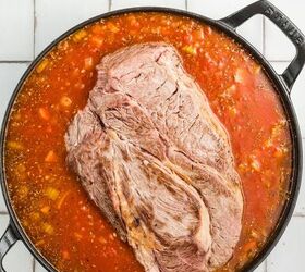 stracotto italian pot roast, A large cut of beef in a pot of tomato sauce with vegetables on a tiled surface