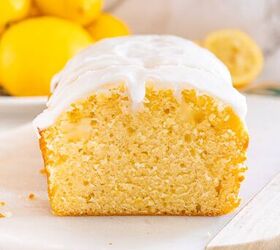 starbucks copycat lemon loaf, A sliced lemon loaf cake with white icing shown on a marble board with fresh lemons in the background