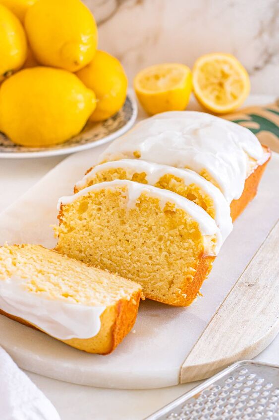starbucks copycat lemon loaf, A loaf of lemon bread with white icing partially sliced sits on a marble board next to fresh lemons