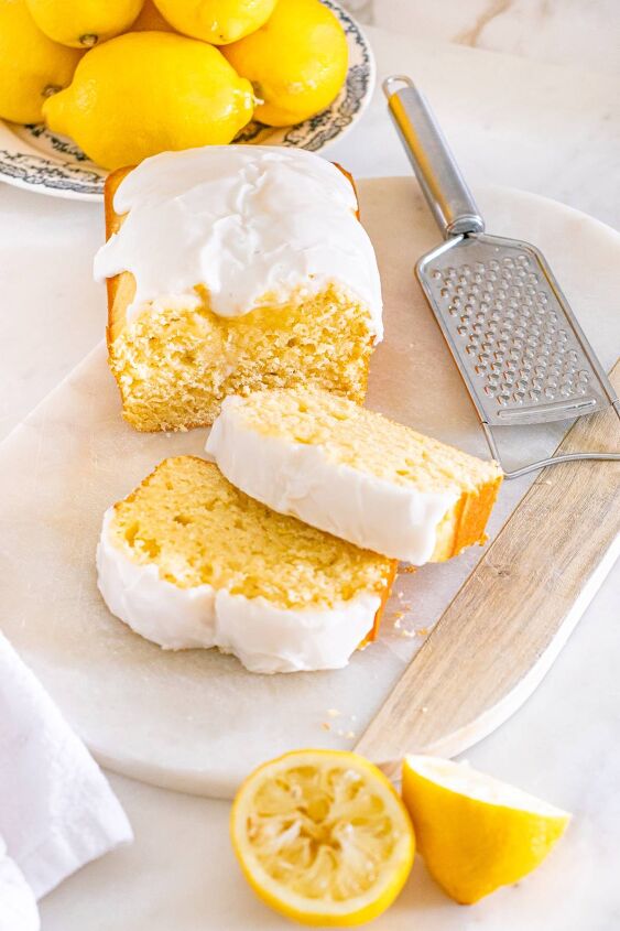 starbucks copycat lemon loaf, A lemon loaf cake with white icing two slices cut surrounded by fresh lemons and a grater on a marble board