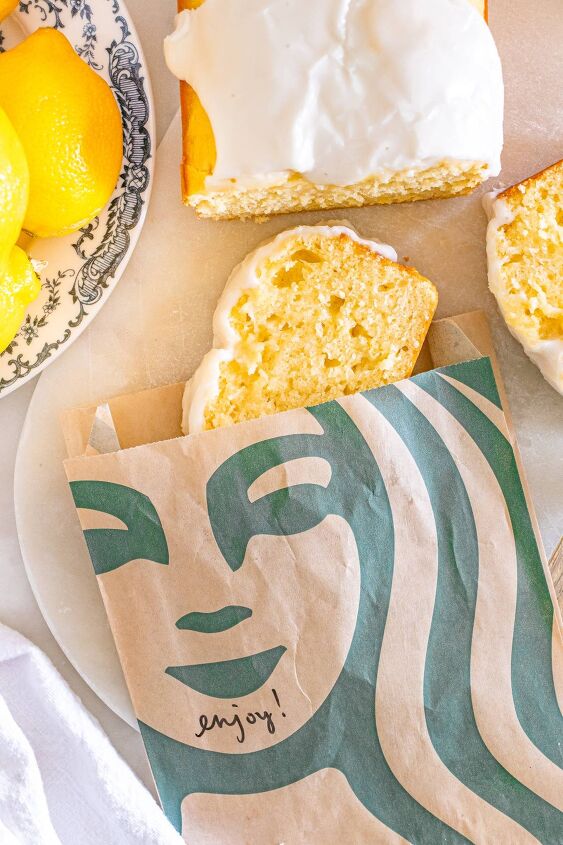 starbucks copycat lemon loaf, A slice of iced lemon loaf in a Starbucks bag beside the rest of the loaf and fresh lemons on a plate