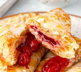 cherry turnovers, A close up of glazed cherry turnovers on a plate The turnovers are flaky and golden brown filled with vibrant red cherry filling A bowl of fresh cherries is blurred in the background