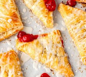 cherry turnovers, Golden brown cherry turnovers with a flaky crust are drizzled with white icing The turnovers are filled with vibrant red cherry filling and scattered on a parchment lined surface