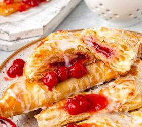 cherry turnovers, A plate of glazed cherry filled pastries with some cut open to reveal the cherry filling A bowl of fresh cherries is in the background A red and white striped cloth is partially visible in the foreground