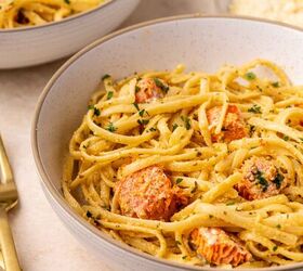 creamy salmon pasta, A close up of a bowl of creamy pasta with chunks of salmon garnished with chopped herbs Another bowl and a plate of grated cheese are in the background alongside gold colored utensils