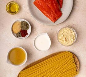 creamy salmon pasta, Uncooked spaghetti raw salmon fillets on a plate bowls of olive oil spices grated cheese cream broth and garlic powder arranged on a light colored countertop
