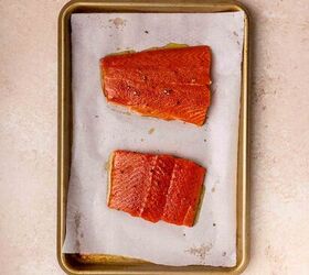 creamy salmon pasta, Two raw salmon fillets on a parchment lined baking sheet placed on a light colored countertop The fillets are seasoned and spaced apart on the tray