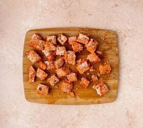 creamy salmon pasta, A wooden cutting board with several cubes of cooked salmon scattered on it set on a light beige countertop