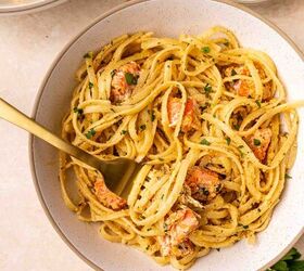 creamy salmon pasta, A bowl of creamy pasta with chunks of salmon garnished with chopped parsley A gold fork is twirled in the pasta and a small bowl of grated cheese and parsley are nearby on a light colored surface