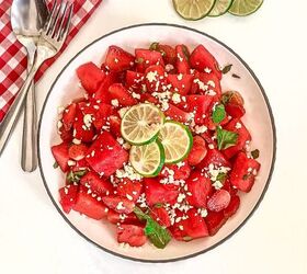 refreshing watermelon strawberry salad recipe, Top down view of watermelon strawberry salad with feta mint and lime in a white bowl beside lime slices and silverware on a white table