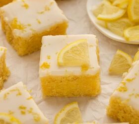 lemon brownies recipe, Lemon brownies with white icing topped with lemon slices and zest arranged on parchment paper with a plate of lemon slices in the background