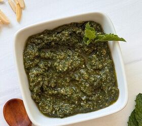 fresh mint pesto vegan gluten free, A square white bowl filled with vibrant mint pesto sauce garnished with a sprig of mint A wooden spoon and slivered almonds rest nearby on a white surface