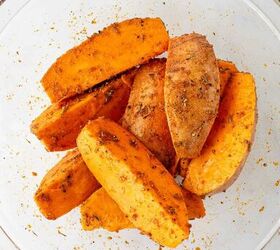 air fryer sweet potato wedges, Sweet potato wedges coated with spices and herbs in a clear glass bowl ready to be baked or cooked