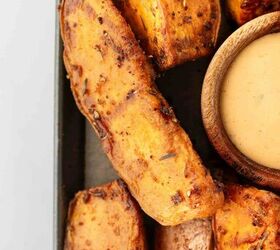 air fryer sweet potato wedges, Close up of seasoned roasted sweet potato wedges arranged next to a small wooden bowl filled with creamy dipping sauce on a tray