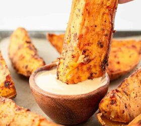 air fryer sweet potato wedges, A hand dips a seasoned sweet potato wedge into a small wooden bowl of creamy dipping sauce with more sweet potato wedges arranged around the bowl