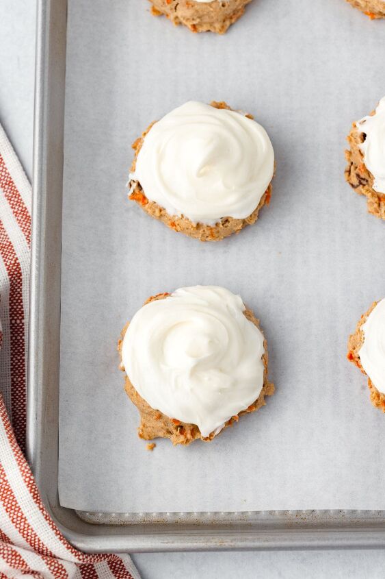 carrot cake cookies, Carrot Cake Cookies with white cream cheese frosting on a parchment lined baking sheet next to a red striped towel