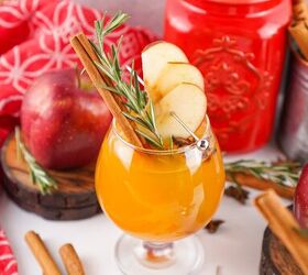 the best fireball apple cider drink for the fall season, Close up angled shot of Fireball apple cider with apple slices rosemary and star anise garnish with red and festive background elements