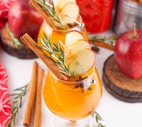 the best fireball apple cider drink for the fall season, Festive scene with two Fireball apple cider cocktails garnished with apple slices and rosemary surrounded by apples cinnamon sticks and rustic props