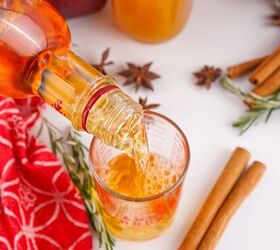the best fireball apple cider drink for the fall season, Fireball cinnamon whisky being poured from the bottle into a measuring cup with apples cinnamon sticks and cider in the background