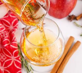 the best fireball apple cider drink for the fall season, Golden Fireball whisky being poured from a measuring cup into a cocktail glass with apples cider and spices on the table
