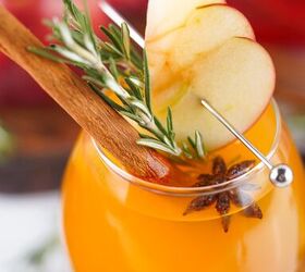 the best fireball apple cider drink for the fall season, Close up of a Fireball apple cider cocktail with apple slices rosemary and cinnamon highlighting the garnish and vibrant orange color