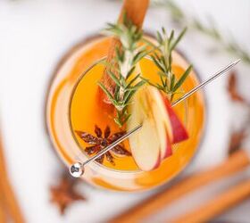 the best fireball apple cider drink for the fall season, Overhead view of a glass of Fireball apple cider garnished with apple slices rosemary star anise and a cinnamon stick