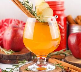 the best fireball apple cider drink for the fall season, Glass of Fireball apple cider with apple slices cinnamon stick rosemary and star anise on a rustic wood coaster surrounded by apples and cinnamon sticks