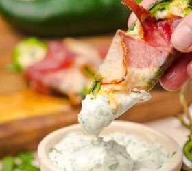 air fryer bacon wrapped jalapeno poppers, A hand dipping a jalapeno popper wrapped with bacon in a bowl of ranch dressing