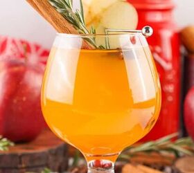 oreo spider cookies recipe for halloween parties, A festive glass of Fireball apple cider garnished with apple slices a cinnamon stick and rosemary set against a cozy fall background with apples and spices