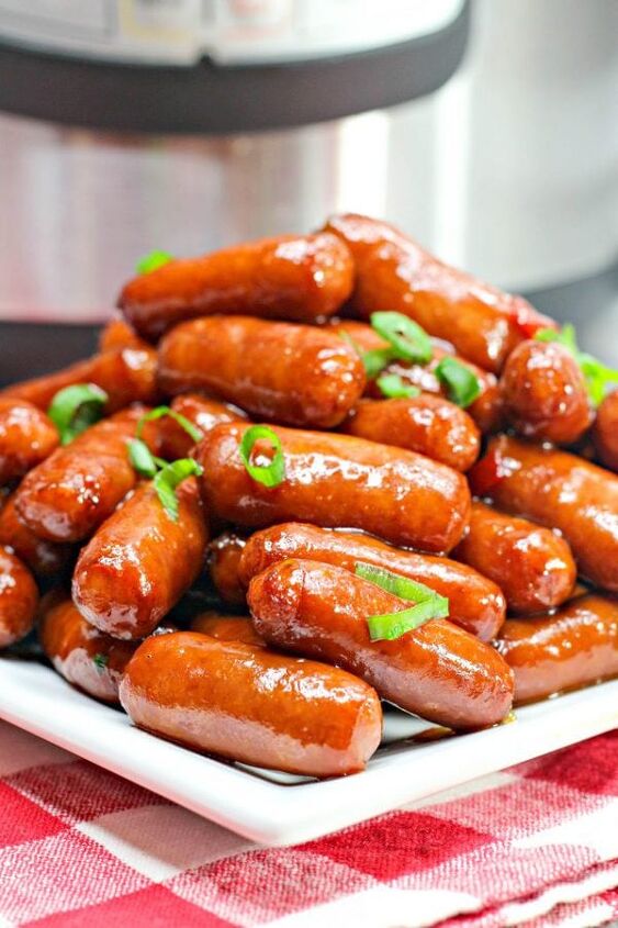 crockpot little smokies, a tall pile of crock pot little smokie sausages in a sweet and tangy sauce garnished with green onions