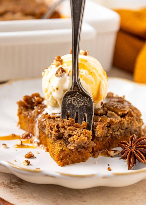 pumpkin dump cake, A fork rests in a slice of spiced pumpkin dump cake topped with a scoop of vanilla ice cream chopped pecans and caramel drizzle on a white plate An anise star garnish sits beside the dessert