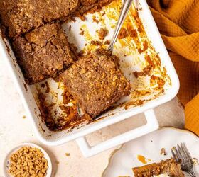 pumpkin dump cake, A white baking dish with pumpkin dump cake one square piece being lifted out with a cake server A plated slice with ice cream and caramel sauce sits nearby with a bowl of chopped nuts and a cinnamon stick on the table