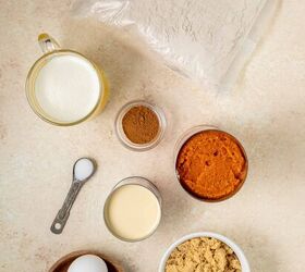 pumpkin dump cake, A flat lay of baking ingredients a bag of cake mix sweetened condensed milk a bowl of brown sugar three eggs a small bowl of melted butter a jar of cinnamon a can of pumpkin puree and a spoon with salt