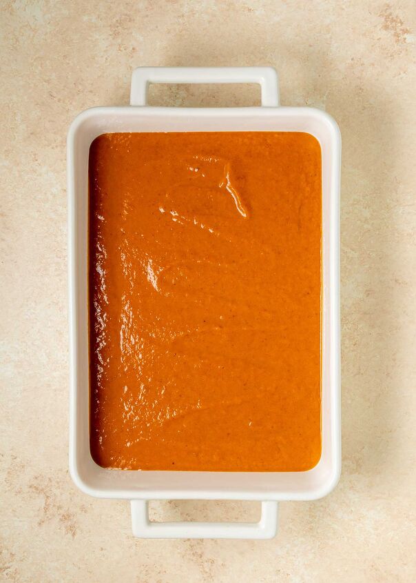 pumpkin dump cake, A white rectangular baking dish filled with a smooth layer of orange brown dump cake batter set on a light beige textured surface