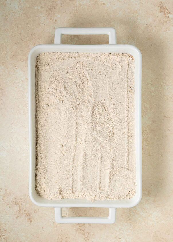 pumpkin dump cake, A white rectangular baking dish topped with cake mix with a lightly smoothed surface sits on a beige countertop