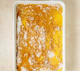 pumpkin dump cake, A rectangular white baking dish filled with an unbaked mixture of yellow melted butter cake mix and some dry ingredients showing a marbled texture on a light colored countertop