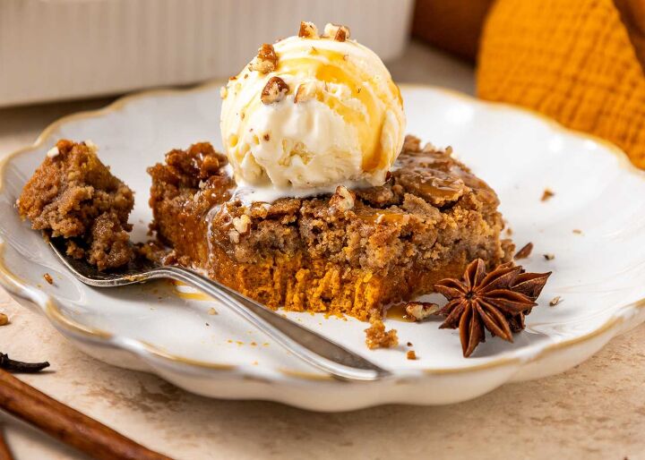 pumpkin dump cake, A slice of pumpkin dump cake topped with a scoop of vanilla ice cream drizzled with caramel sauce and garnished with chopped nuts and a star anise on a decorative white plate A fork holds a bite of the cake