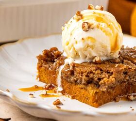 pumpkin dump cake, A slice of pumpkin dump cake topped with a scoop of vanilla ice cream toffee bits and caramel drizzle on a white plate A pan of more dessert and a cinnamon stick are in the background
