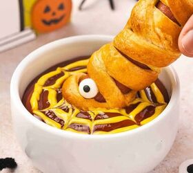 spooky cute air fryer mummy hot dogs kids will love, Close up of a golden Air Fryer Mummy Hot Dog being dipped into ketchup and mustard showing candy eyes and crescent roll bandages