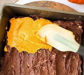 pumpkin cheesecake brownies recipe for fall desserts, Pumpkin mixture being spread over chocolate brownie batter in a baking pan with a spatula