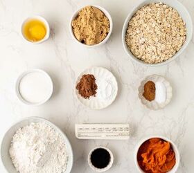 pumpkin oatmeal cookies, Top down view of baking ingredients in bowls and plates on a marble surface including an egg brown sugar oats flour pumpkin puree spices vanilla extract butter and a small bowl of milk