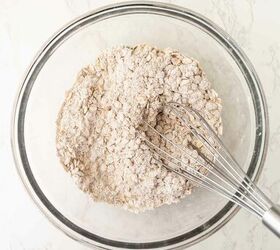 pumpkin oatmeal cookies, A glass bowl containing a mixture of flour and oats being whisked with a metal whisk on a light colored marble surface