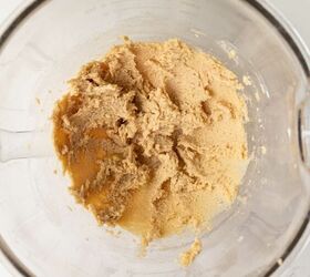 pumpkin oatmeal cookies, A glass mixing bowl containing light brown cookie dough mixture on a white marble surface viewed from above