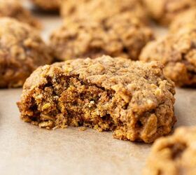 pumpkin oatmeal cookies, A close up of a soft chewy pumpkin oatmeal cookie with a bite taken out showing its textured inside More cookies are blurred in the background all resting on parchment paper