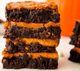 perfectly moist cream cheese pumpkin bread recipe, Stack of homemade pumpkin cheesecake brownies with fudgy chocolate layers surrounded by white chocolate chips with a blurred pumpkin in the background