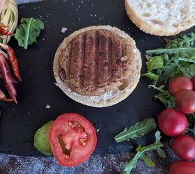 spicy jackfruit and red kidney bean burgers, A plant based kidney bean burger with a jackfruit served in a whole grain bun The burger is open and on the table next to the bun is fresh avocado slices a thick slice of tomato arugula cherry tomatoes and dried chili peppers The burger is placed on a black slate surface