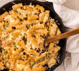 french onion pasta, A skillet filled with rigatoni pasta topped with melted cheese and fresh thymne with a wooden spoon resting inside and a white towel wrapped around the skillet handle