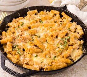 french onion pasta, A cast iron skillet filled with baked rigatoni pasta covered in melted cheese and onions and garnished with fresh herbs set on a light colored table next to gold utensils and a white napkin