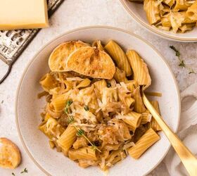 french onion pasta, A bowl of rigatoni pasta topped with caramelized onions grated cheese fresh thyme and slices of toasted baguette with a gold fork beside it Another bowl and cheese grater are visible in the background