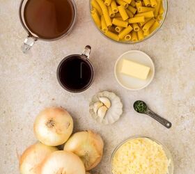 french onion pasta, A top down view of ingredients on a light counter several yellow onions dry pasta a bowl of shredded cheese a small bowl of butter garlic cloves a measuring spoon of thyme red wine and beef broth